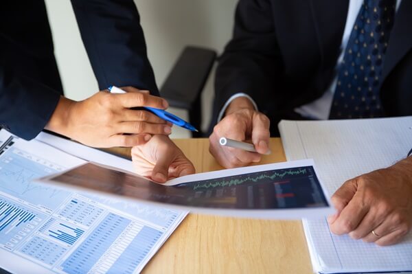 investor-broker-discussing-trading-strategy-holding-papers-with-financial-charts-pens-cropped-shot-broker-job-investment-concept